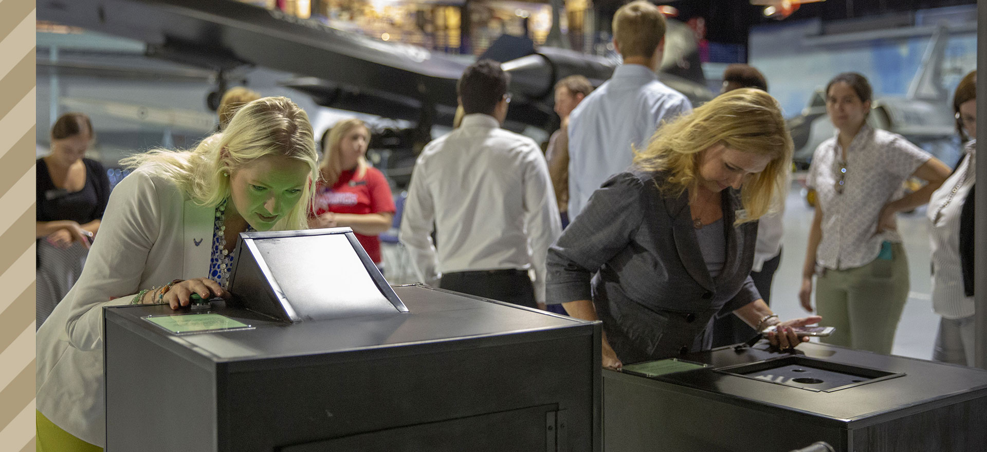 Two visitors stare into viewers of large gray boxes. One woman's face glows green from the reflected light.