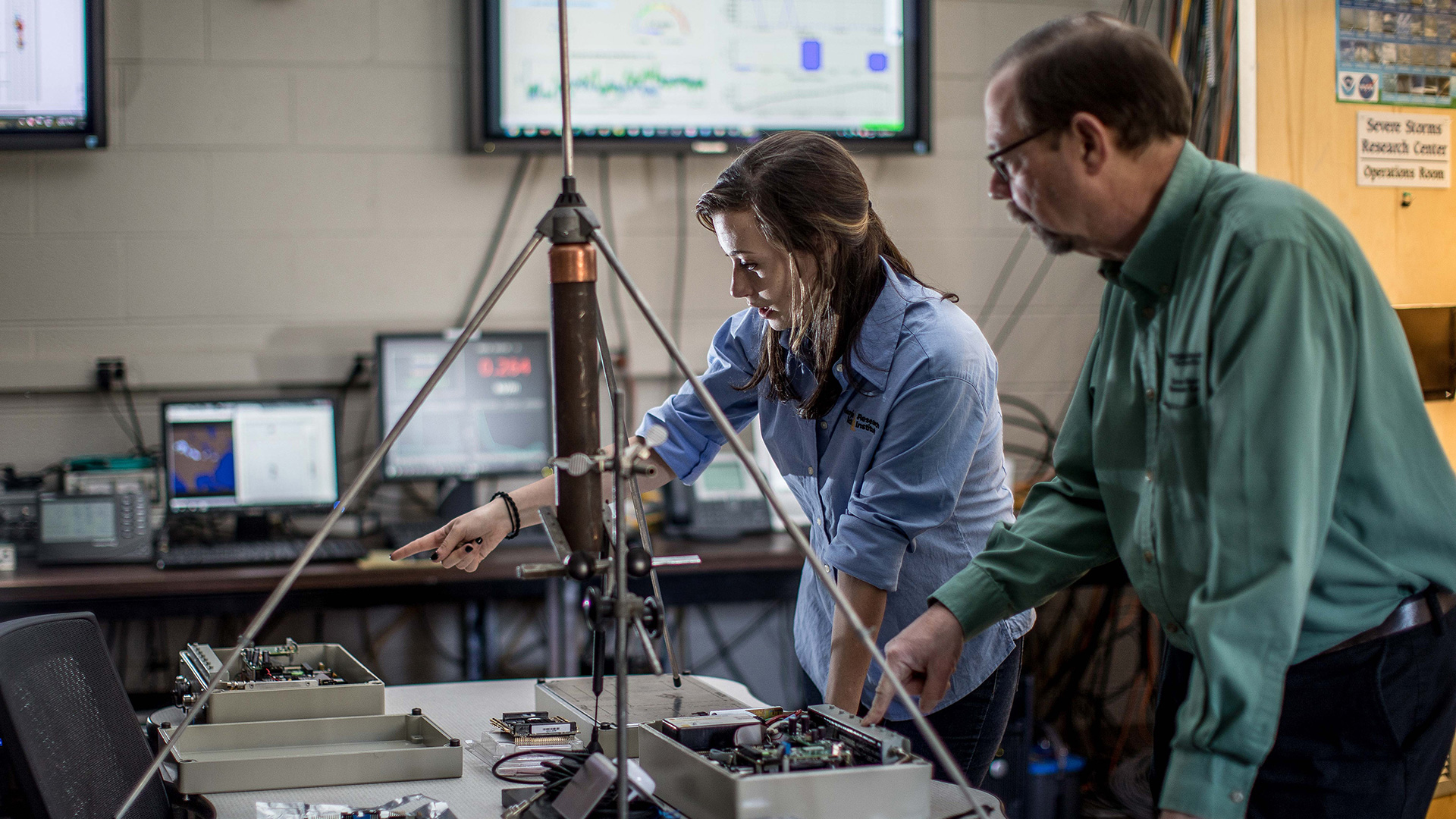 photo: a young woman and older man standing at a table containing weather instruments.