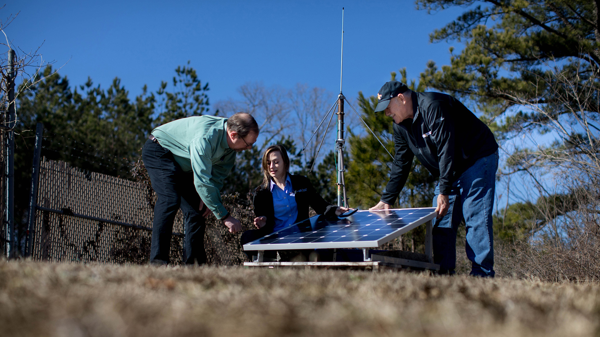 photo: two men and one woman, working outdoors in a field on a crisp Fall day, examine weather equipment.