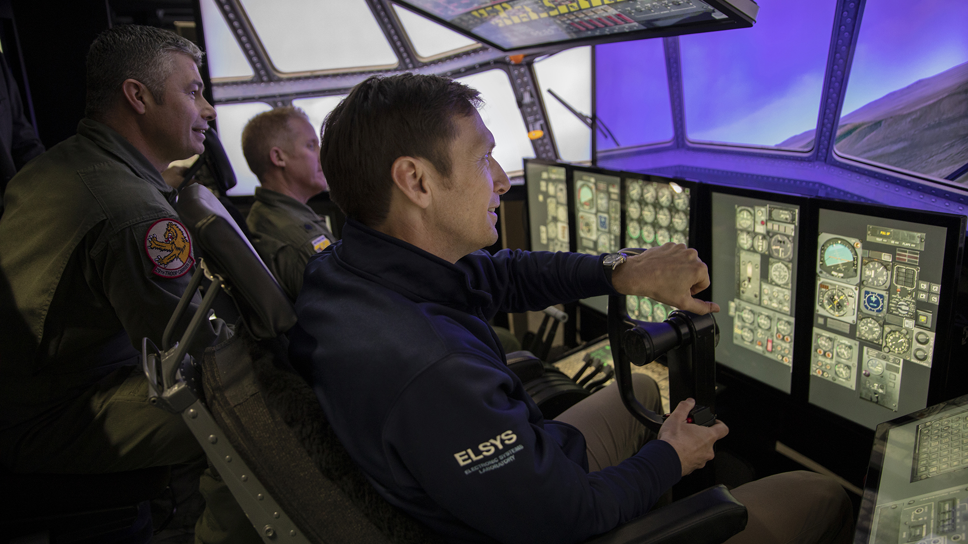 photo - three men sitting in cockpit of flight simulator