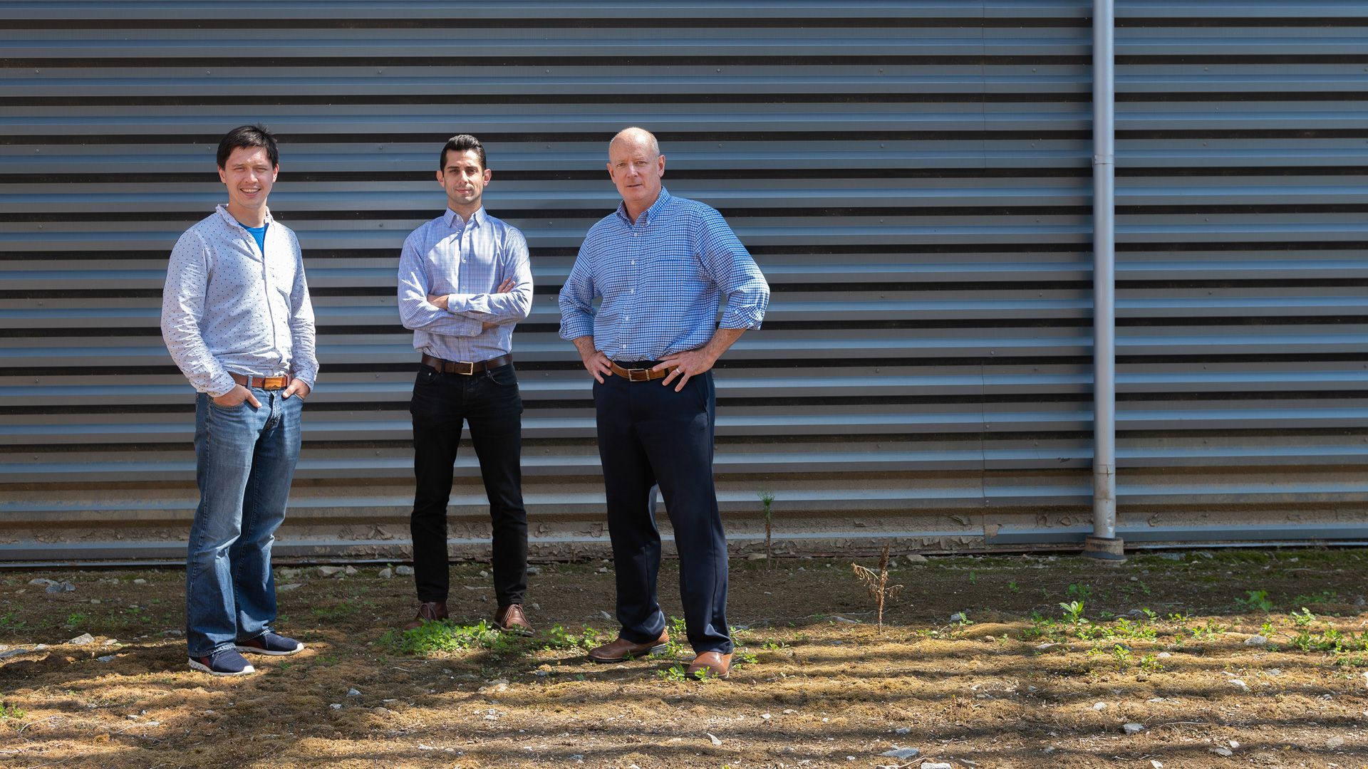 photo: three men standing in front of a corrugated metal building.