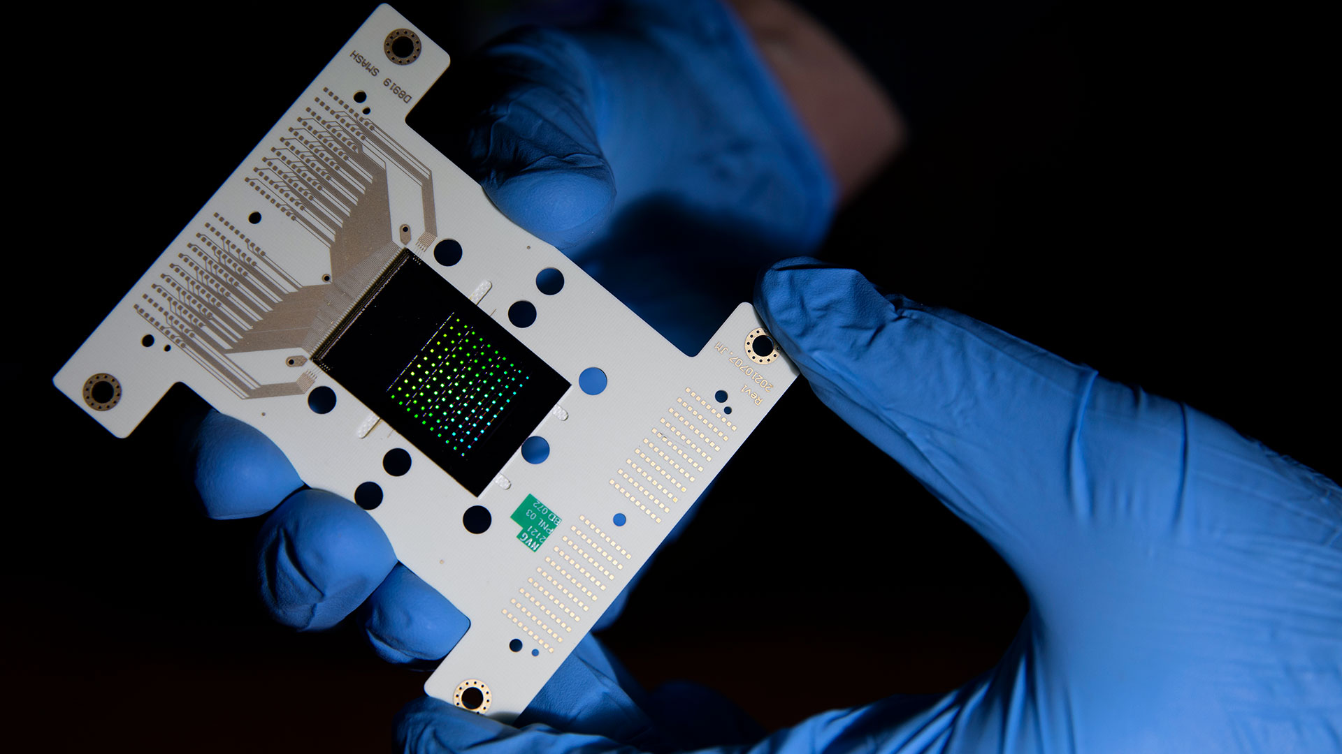 Researcher's gloved hands hold microchip device.