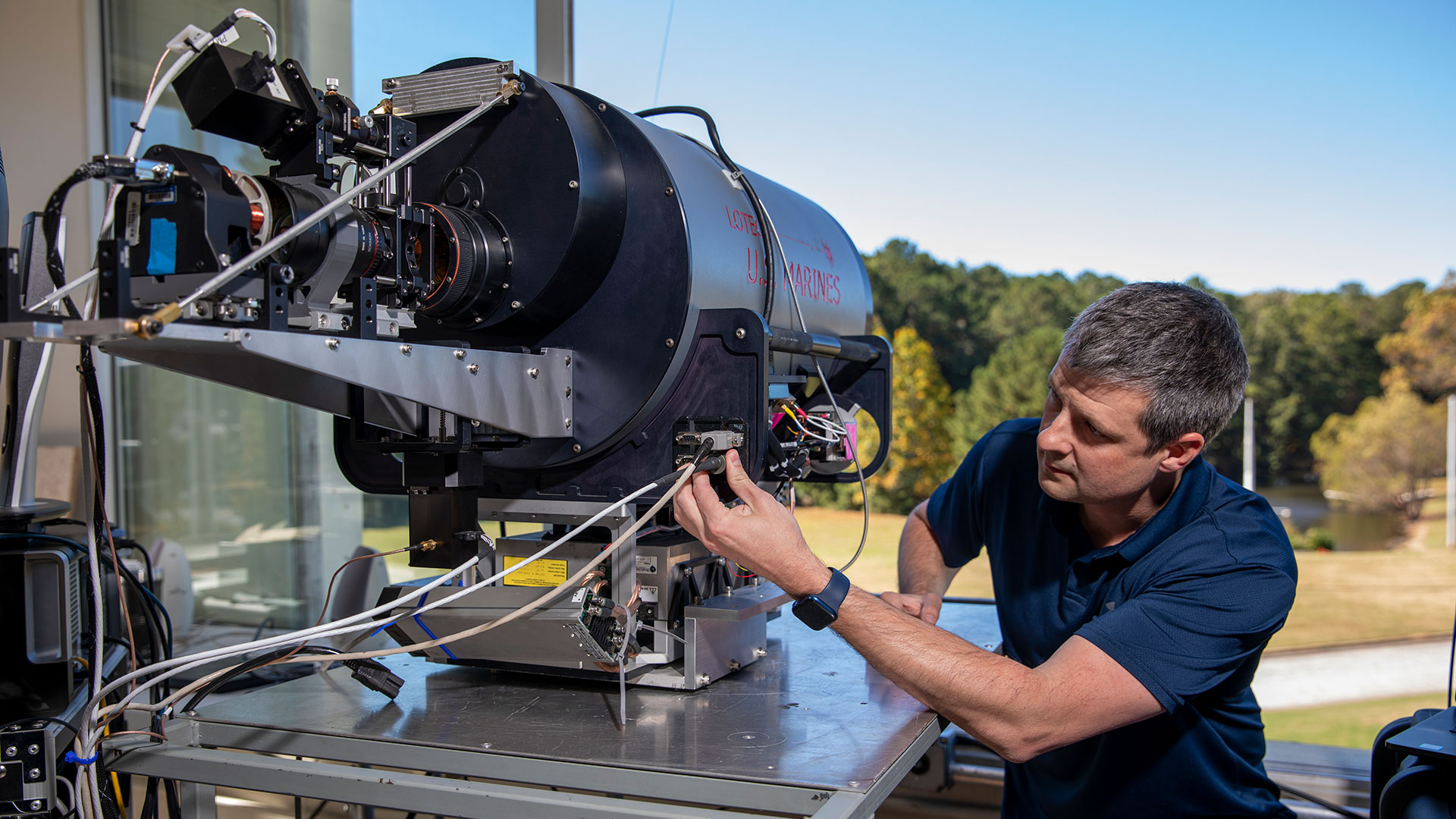 Male researcher examines large round metal Lidar system device.