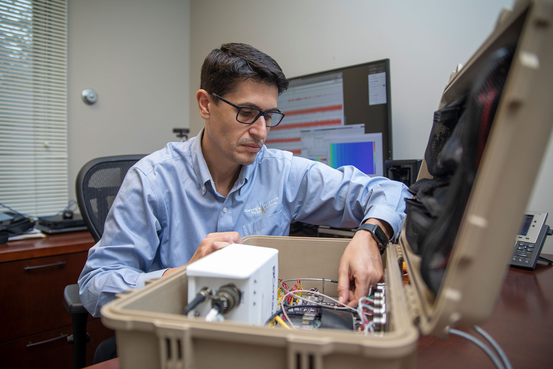 Researcher sitting at desk with large plastic case open to reveal electronics inside.