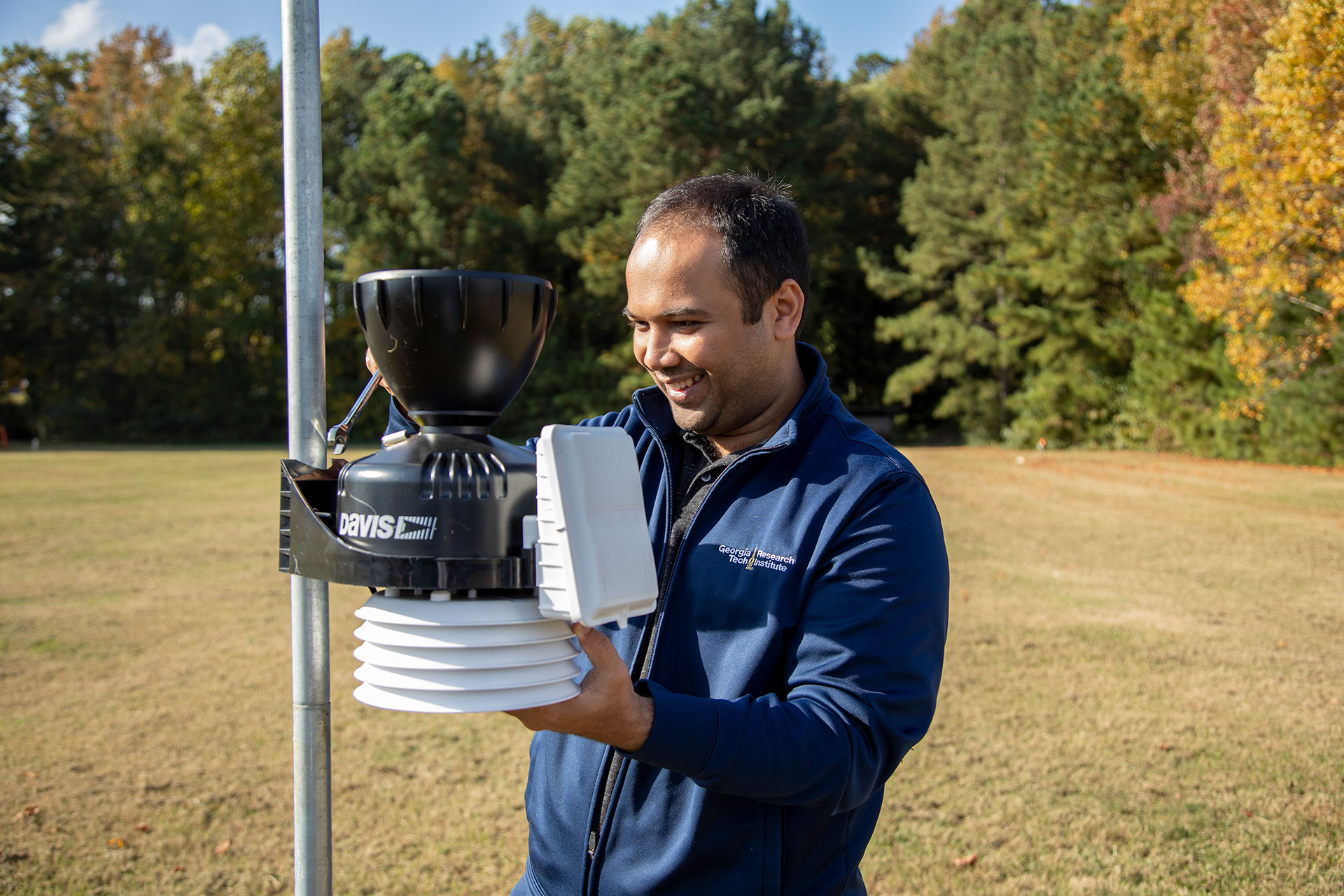 Researcher standing outdoors adjusting device attached to pole.