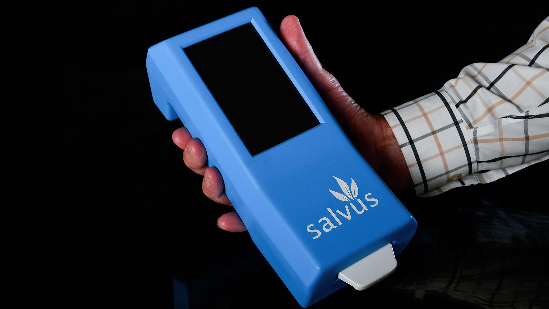 Hand holding rectangular blue plastic device with screen on front.