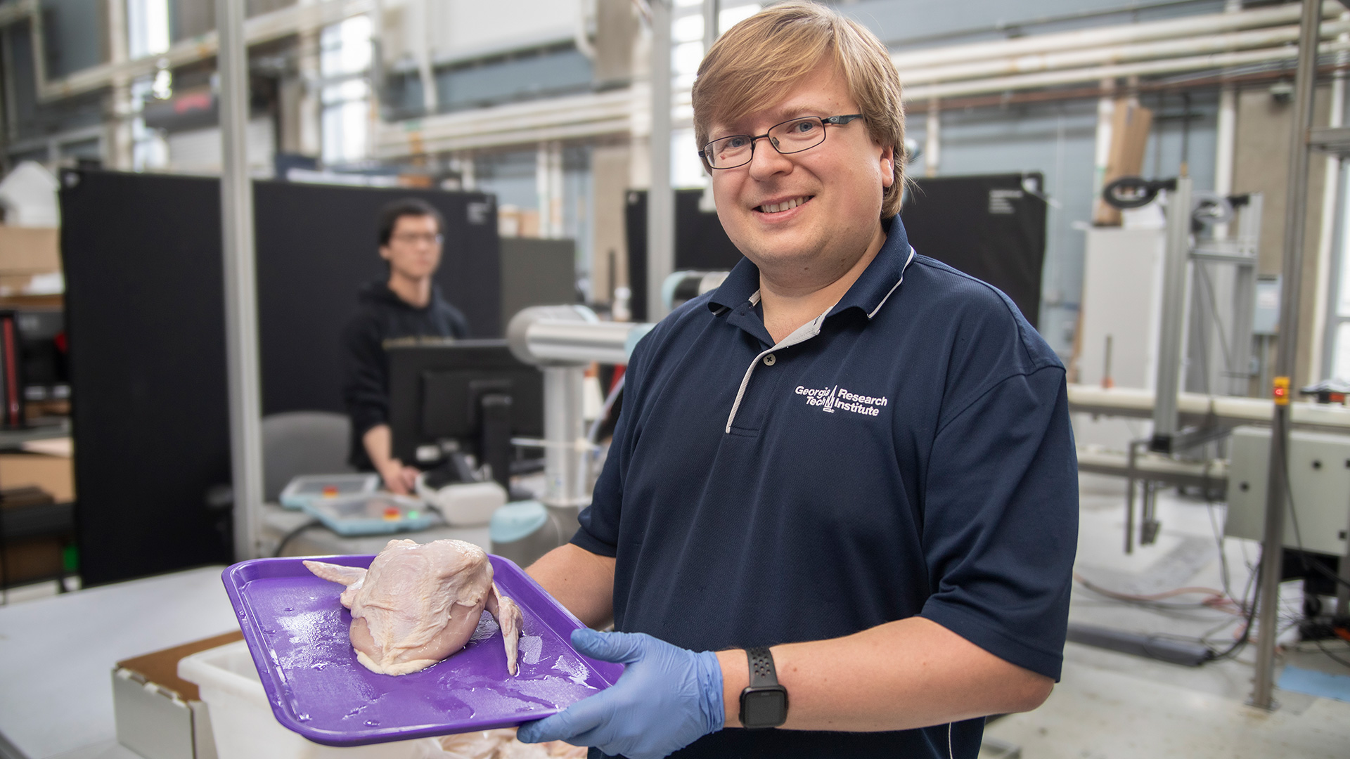 Young male research in lab holding plastic tray with raw chicken.