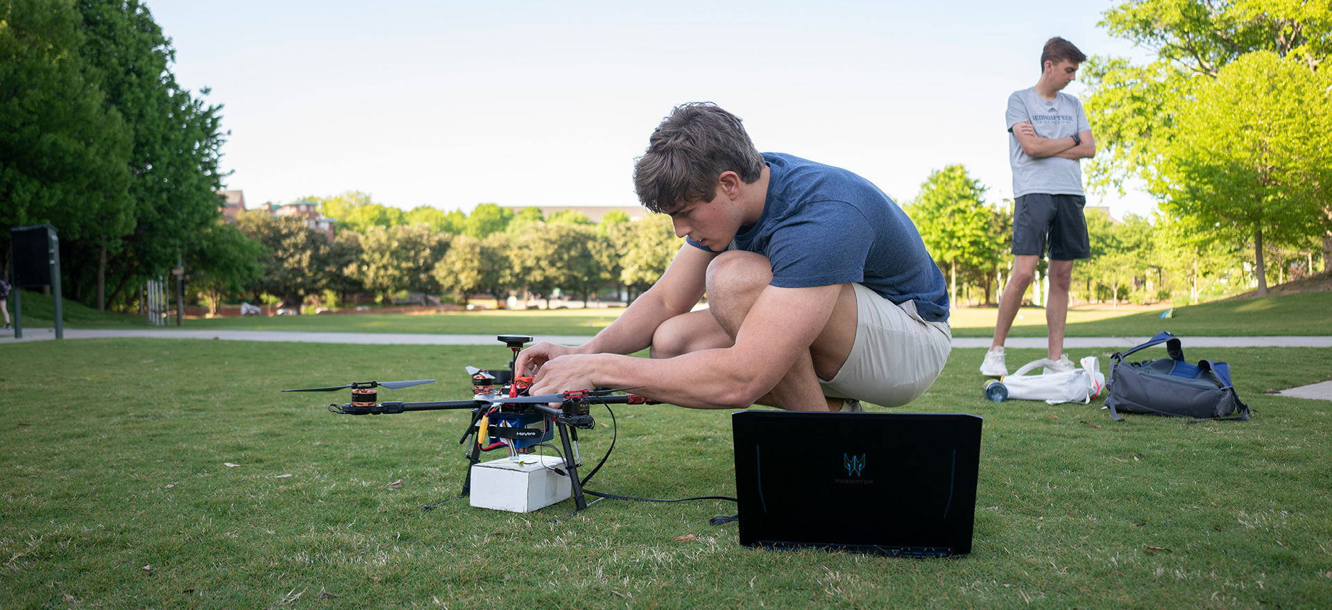 Student kneeling on grass adjusting small drone.