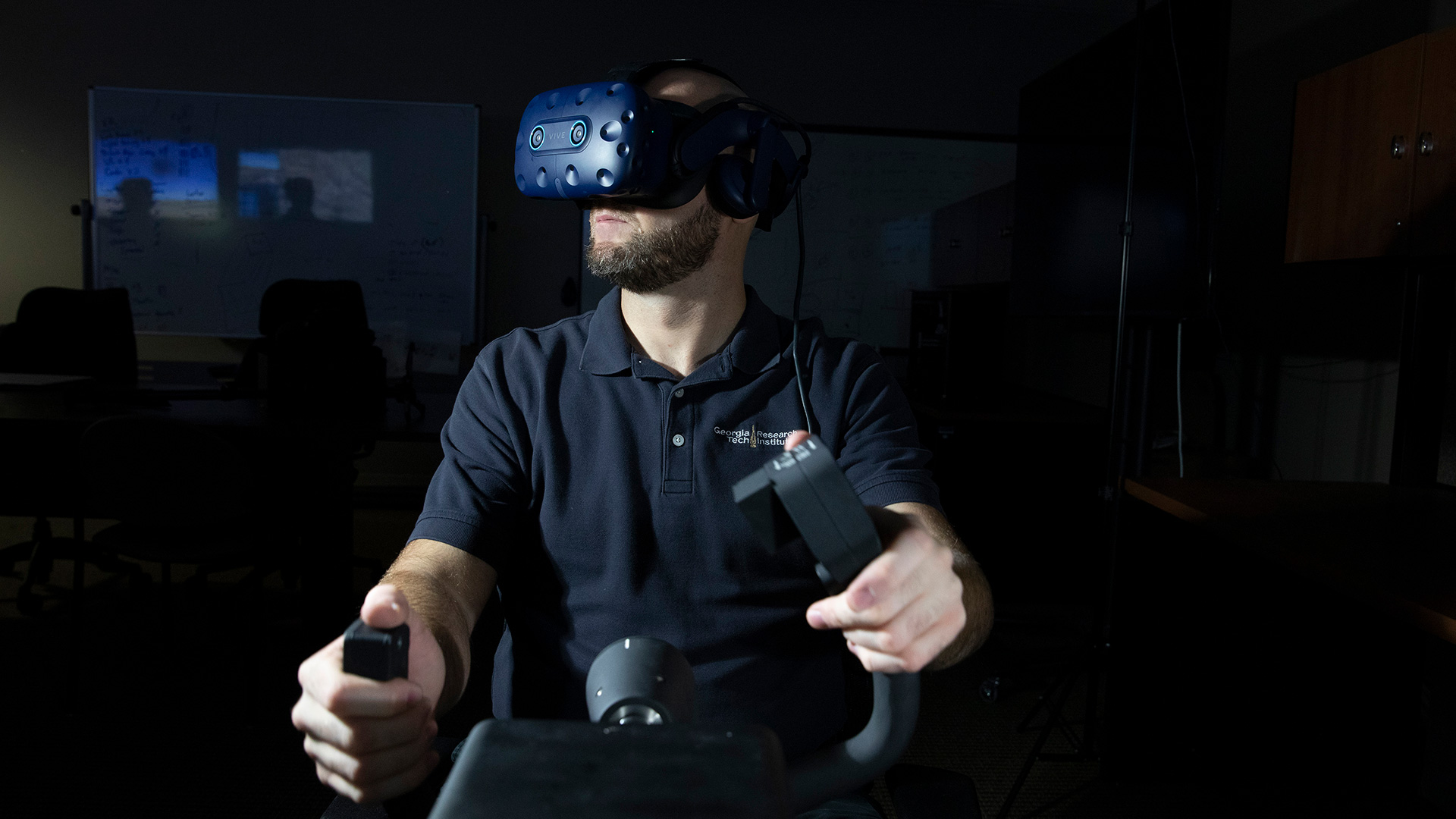 Front view of male researcher wearing VR goggles with hands on flight controls, in a darkened room