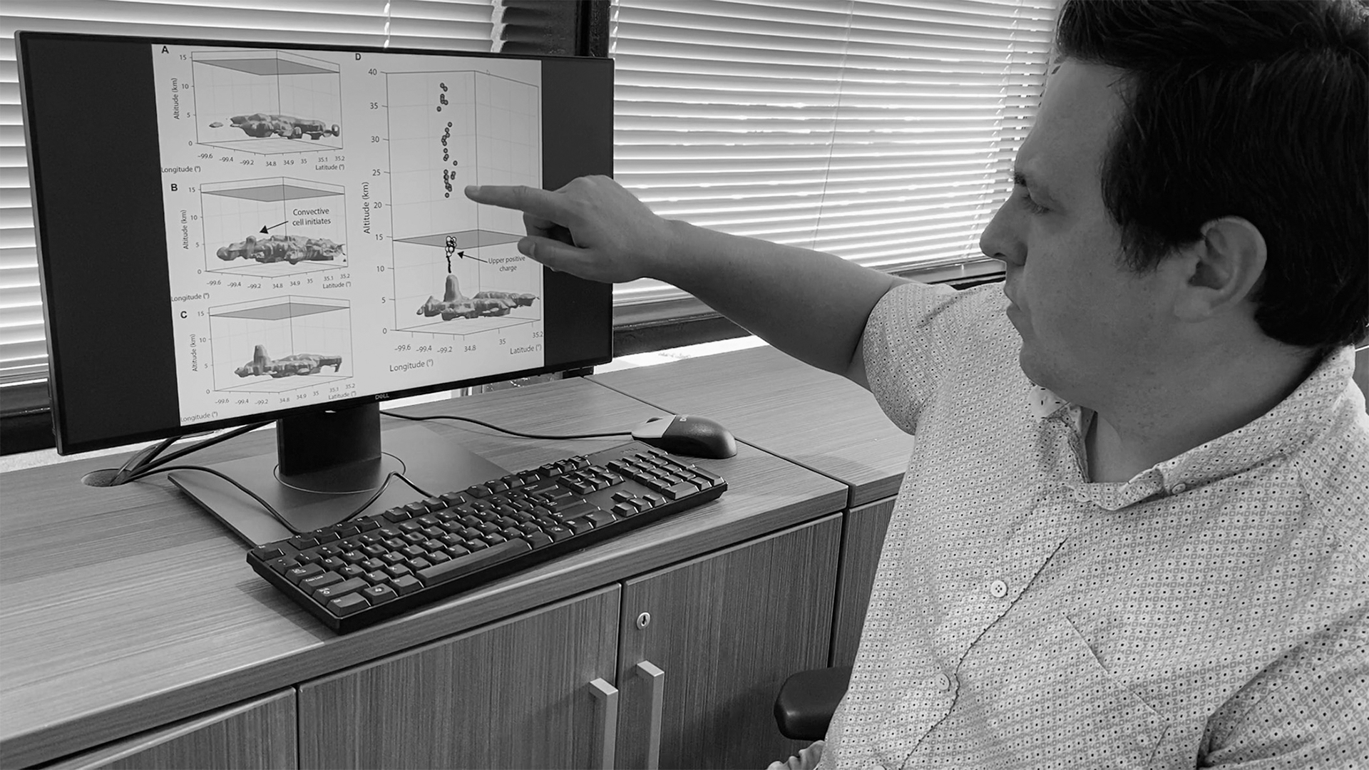 Researcher at desk pointing at computer monitor showing diagrams