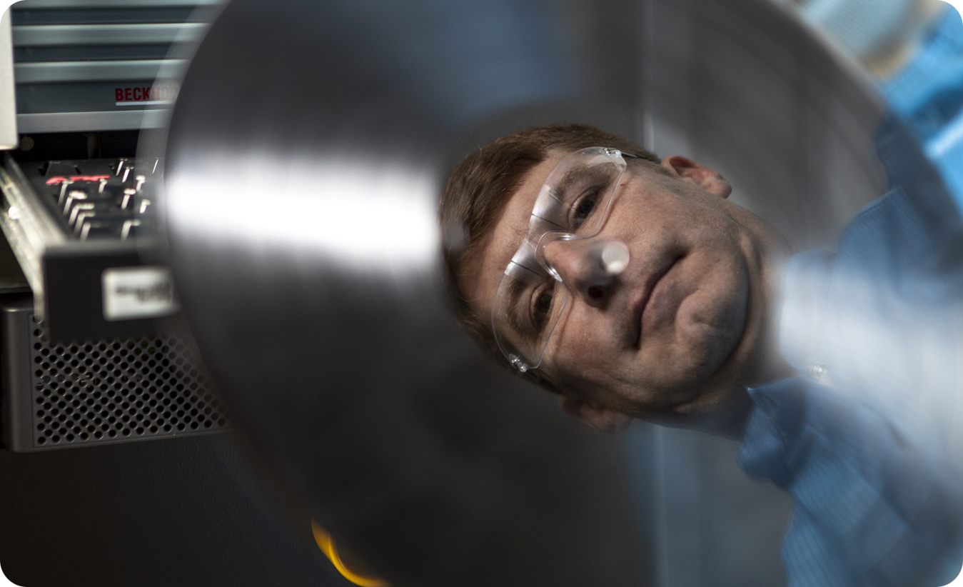 Reflection in dark disc of a man in full protective gear in a clean room.