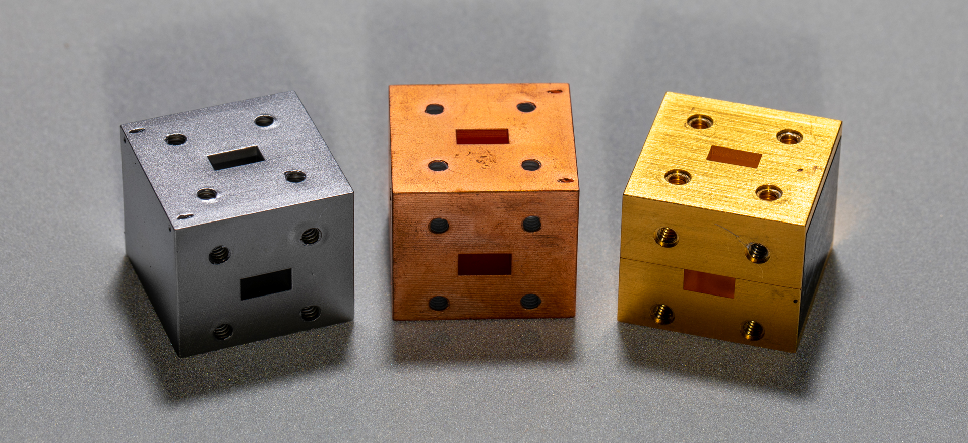 Three small 3D printed cubes on table. The first is silver in color, the second is copper color, the third is gold color.