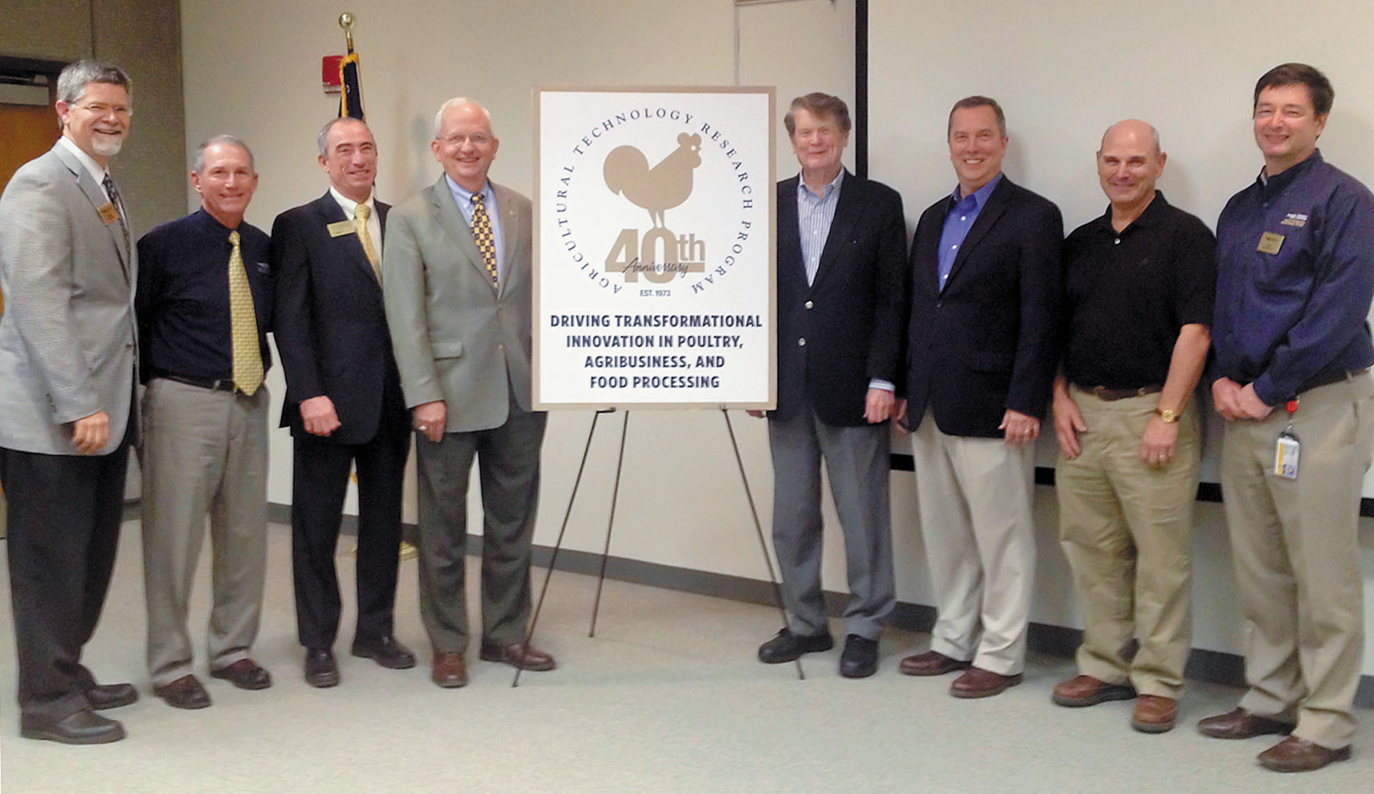 Group of men standing on each side of an easel displaying a 40th Anniversary message.