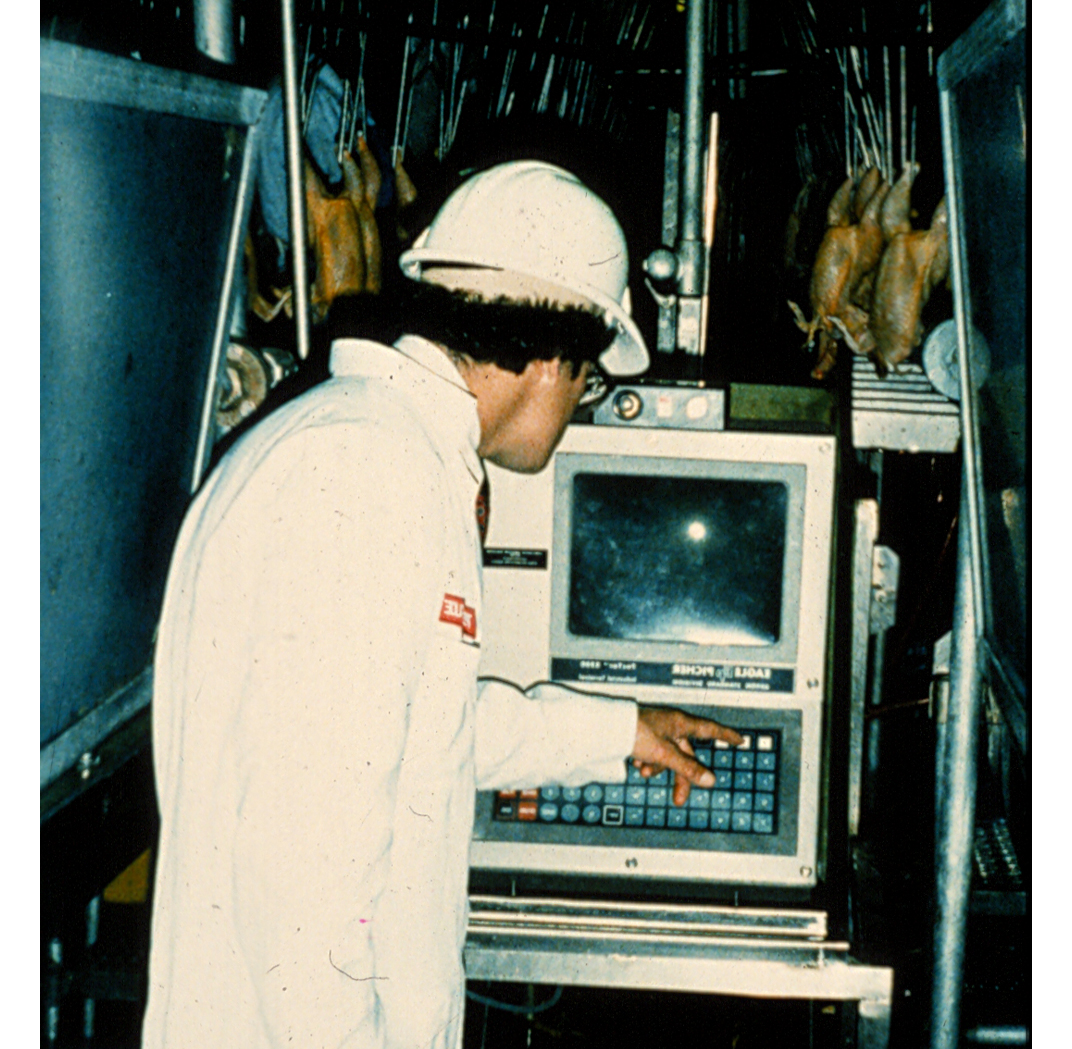 Vintage photo of male technician dressed in lab coat and hard hat working at an early computer