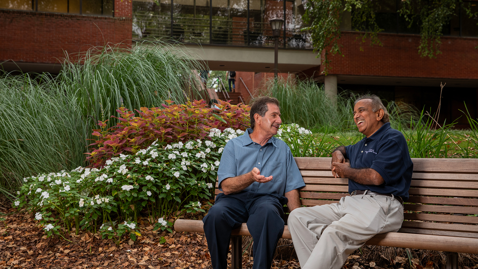 Two senior men (one black, one white) sit and talk on an outdoor bench on the Georgia Tech campus
