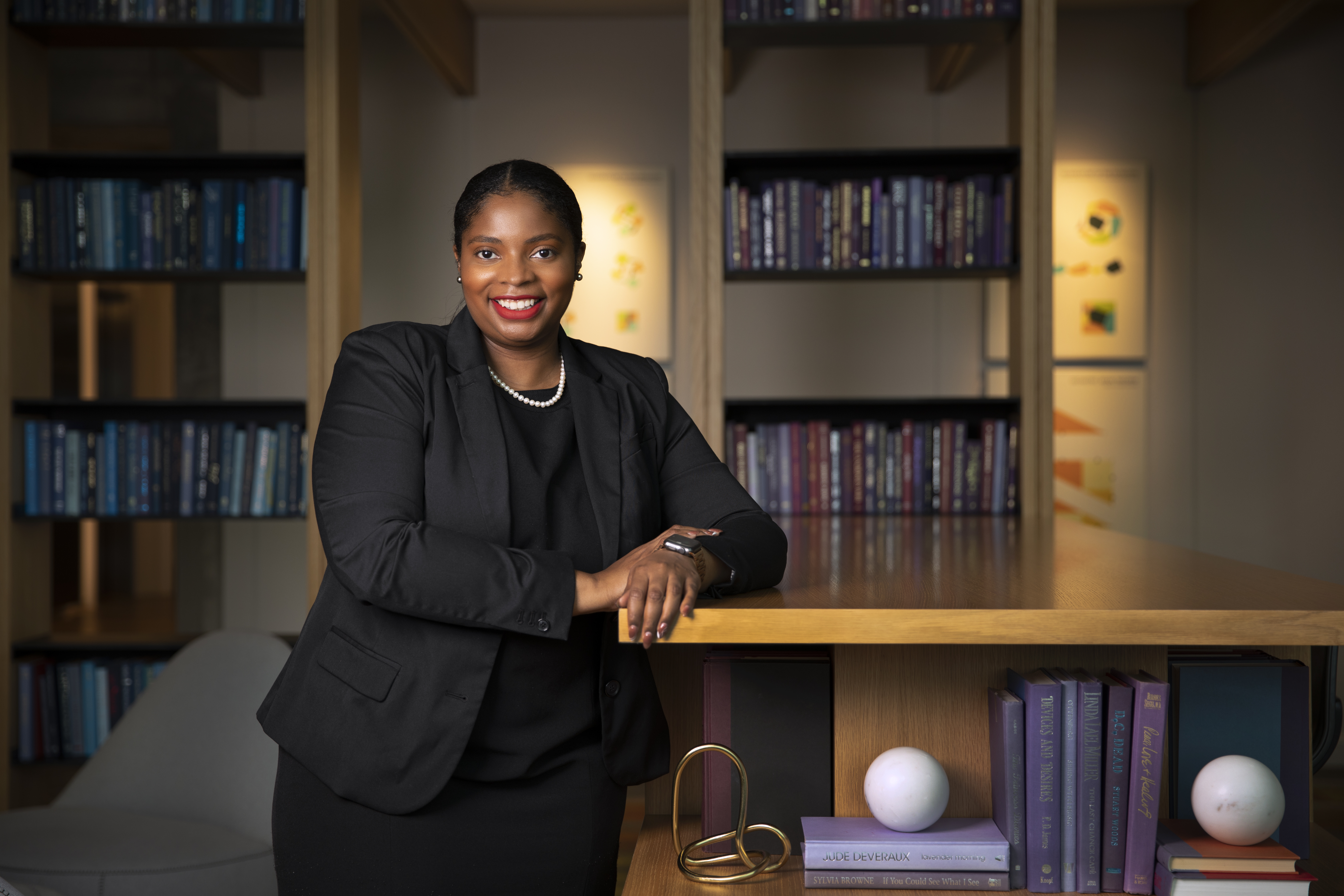 Brittney Odoi is shown standing in a black suit, learning against a table.