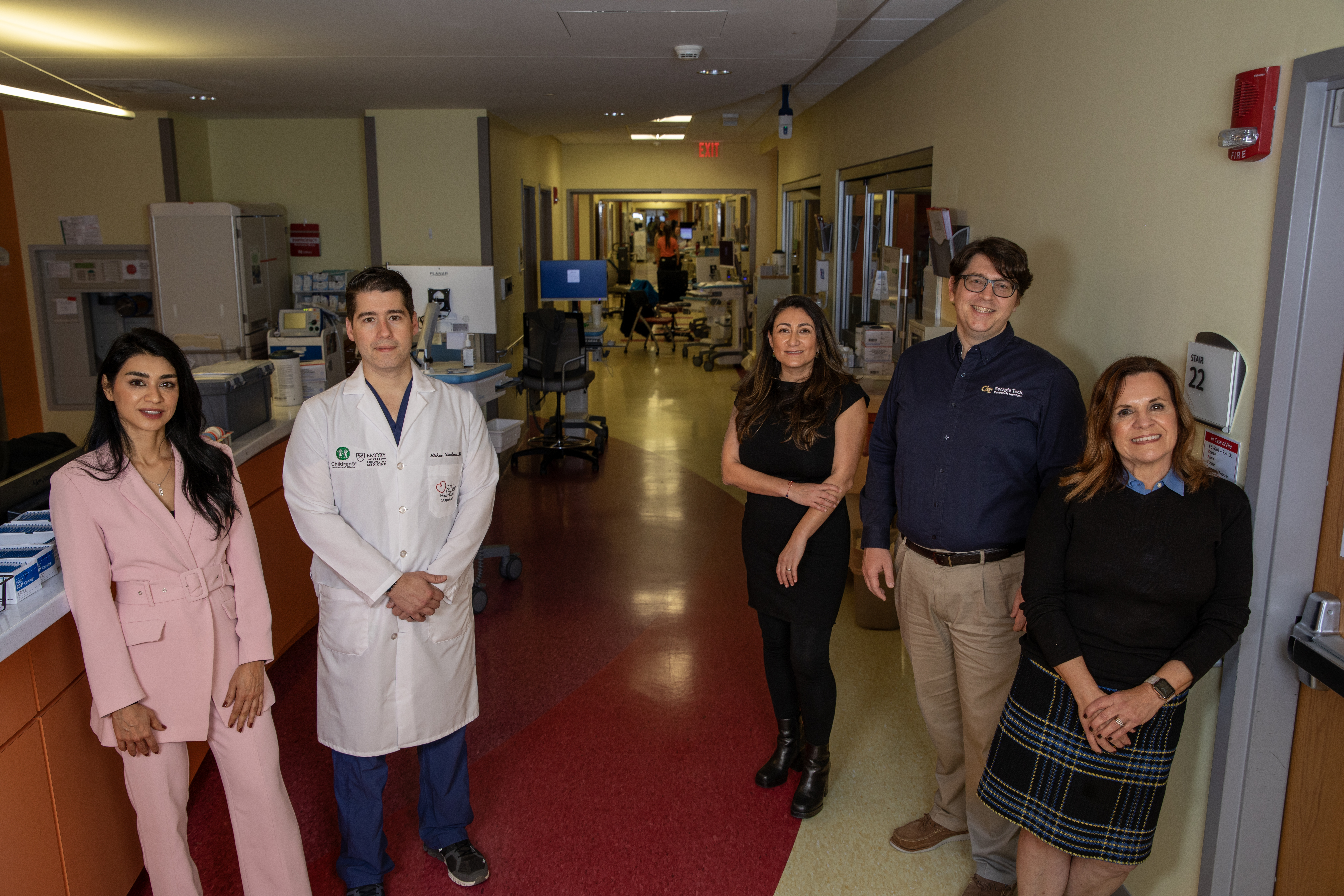 Five people standing near hospital desk looking at camera, three women and two men