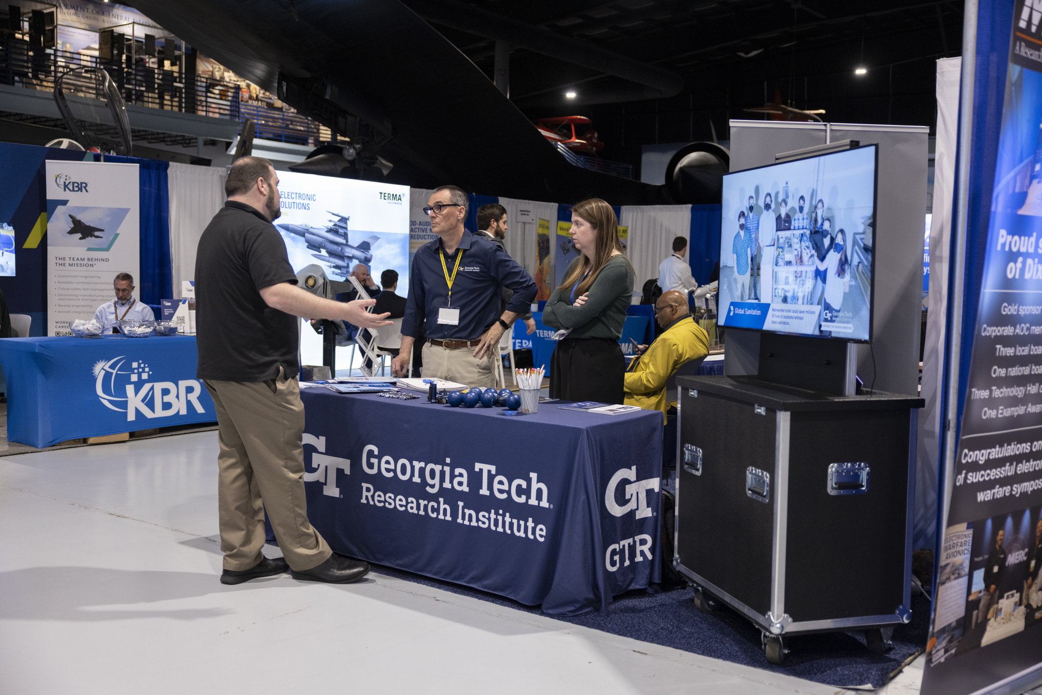 At the Dixie Crow 50th Symposium, Lee Evans and Sara Blevins greet a booth visitor. (Photo Credit: Christopher J. Moore, GTRI)