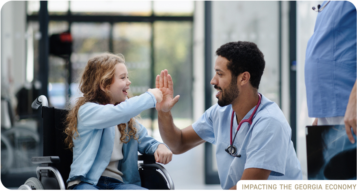 Black male medical professional gives a young blond girl in a wheelchair a high five