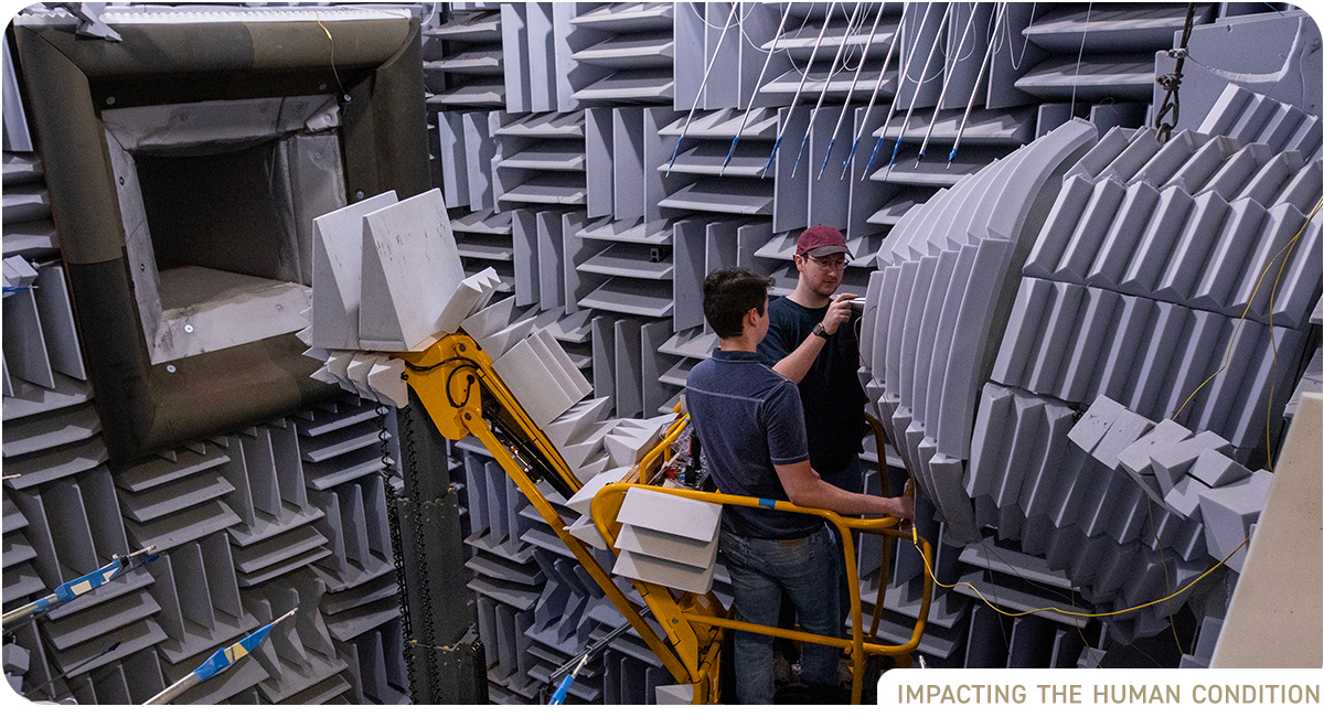 Two male researchers in sound chamber examining a nozzle device