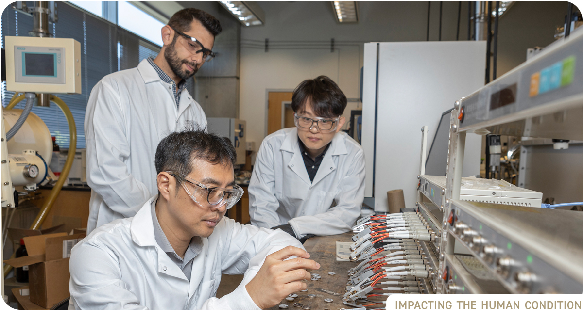 Three male researchers in lab with battery testing device