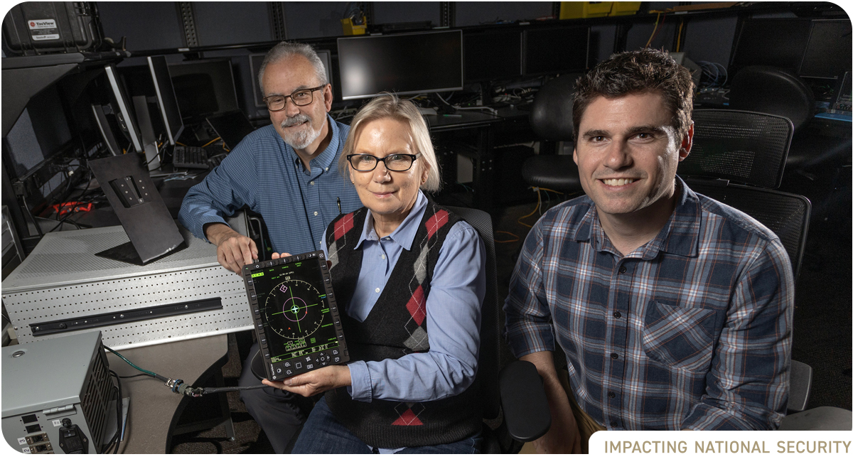 photo: Two male and one female researcher seated in lab. Female researcher in center holds device.