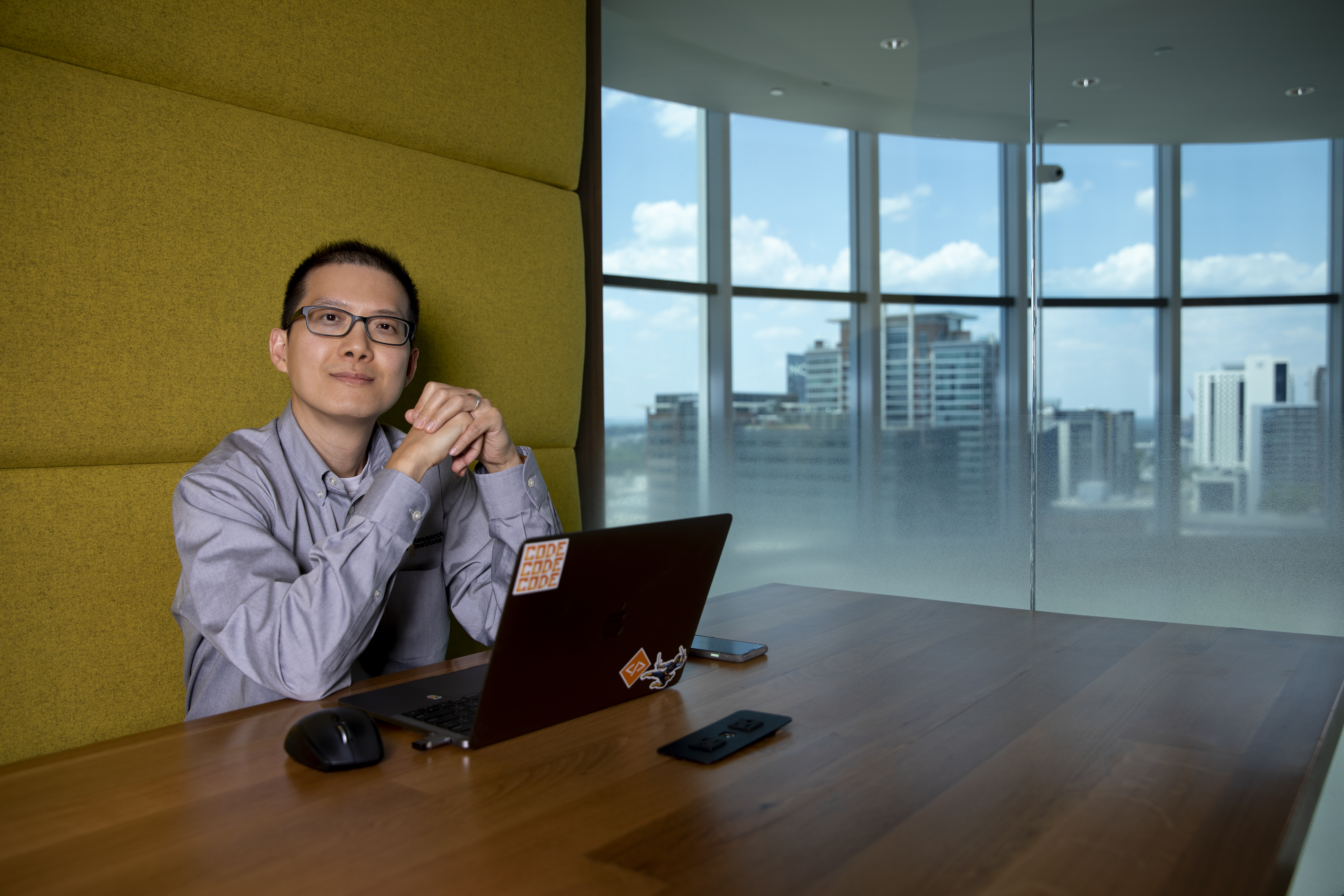 David Tran sits at a wooden table with his hands interlocked over his computer. (Credit: Sean McNeil)