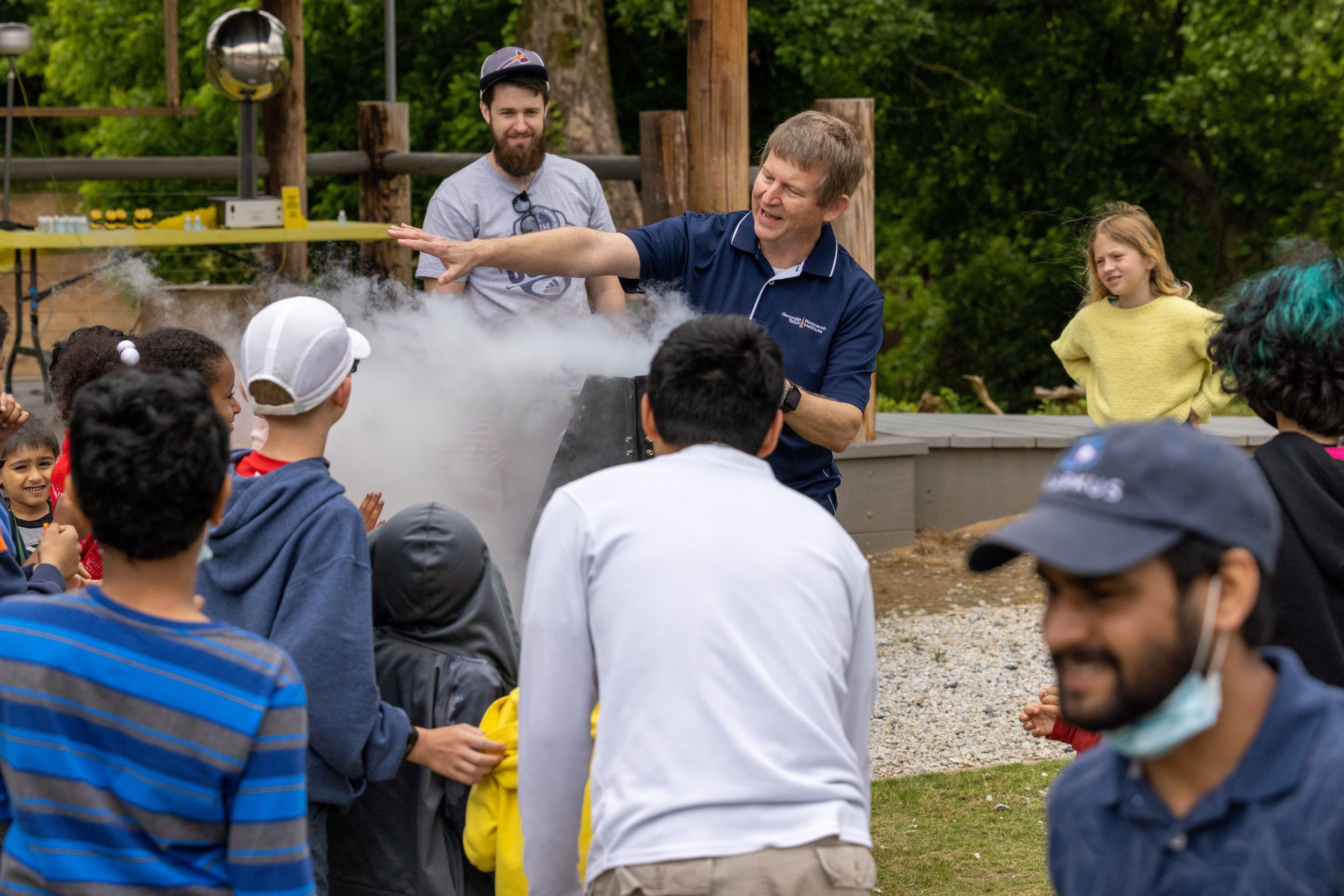 A group of kids huddled around a cloud of fog created by the liquid nitrogen demonstration.