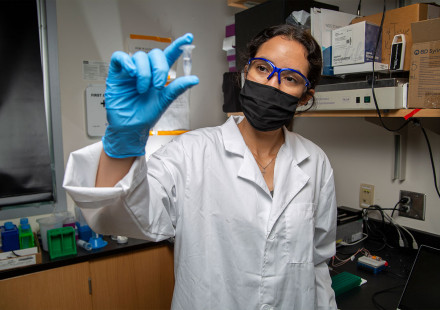 Woman research holds up small vile of clear liquid.