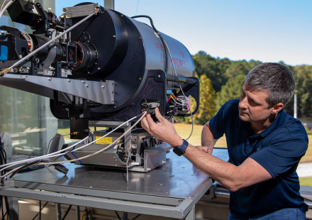 Male researcher examines large round metal Lidar system device.