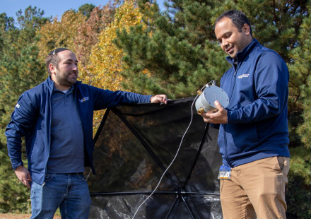 Two researchers outdoors setting up umbrella like device.