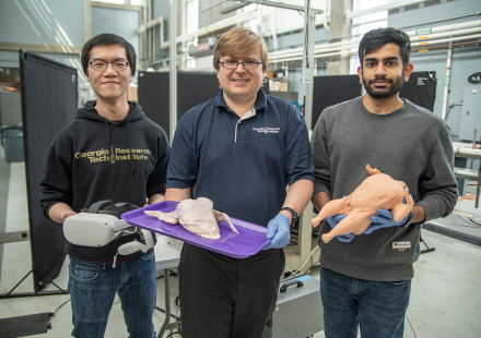 Three young male researchers standing side by side, left one holding VR glasses, center one holding raw whole chicken, right one holding rubber chicken 