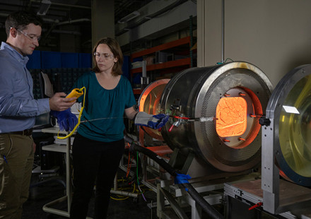 Two researchers stand near a large metal instrument with center glowing red hot