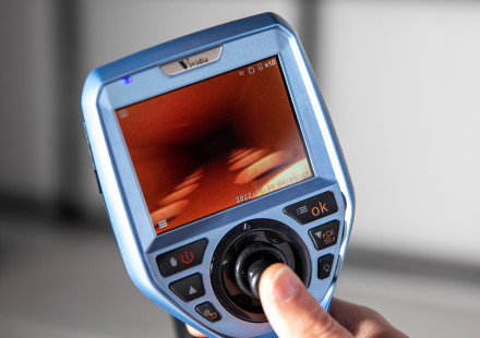 Researcher's hand holds measuring device that contains a display screen and control buttons.