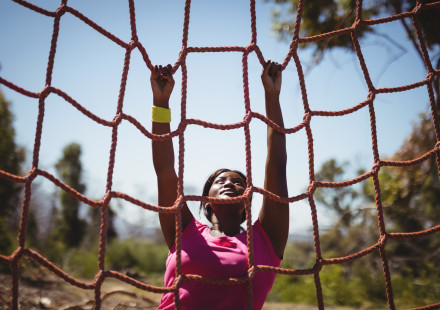 Determined woman climbing a net during obstacle course. Credit iStock.comWavebreakmedia