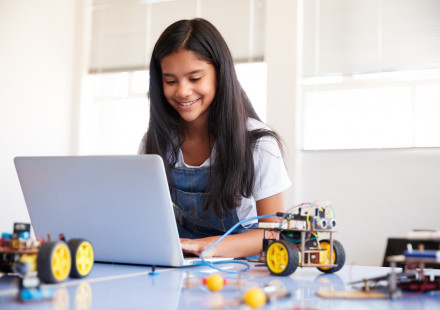 Female student sitting at a computer building and programming robot vehicle