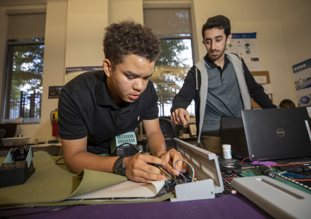 A high school student completing a STEM project with instructor looking over his shoulder. 
