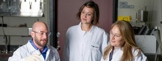Three GTRI researchers in white lab coats looking at technology