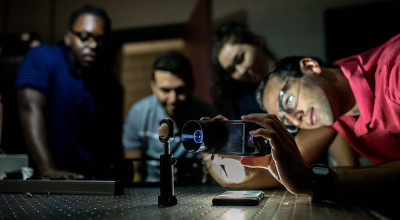 Photo of four interns gathered around a lab table, all appearing to study a device.